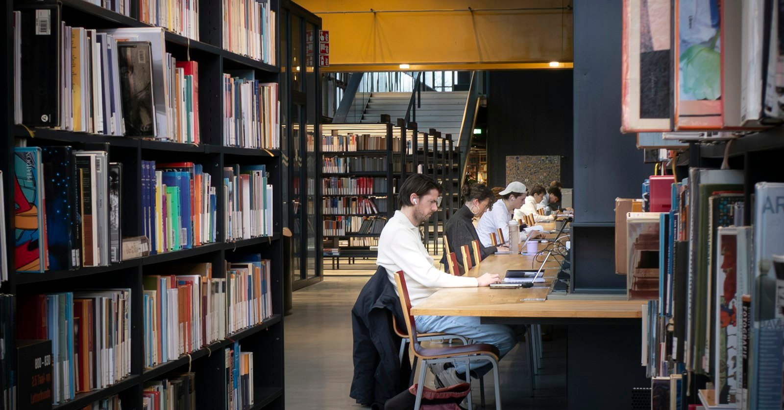 A student working at a desk covered in books and a laptop.