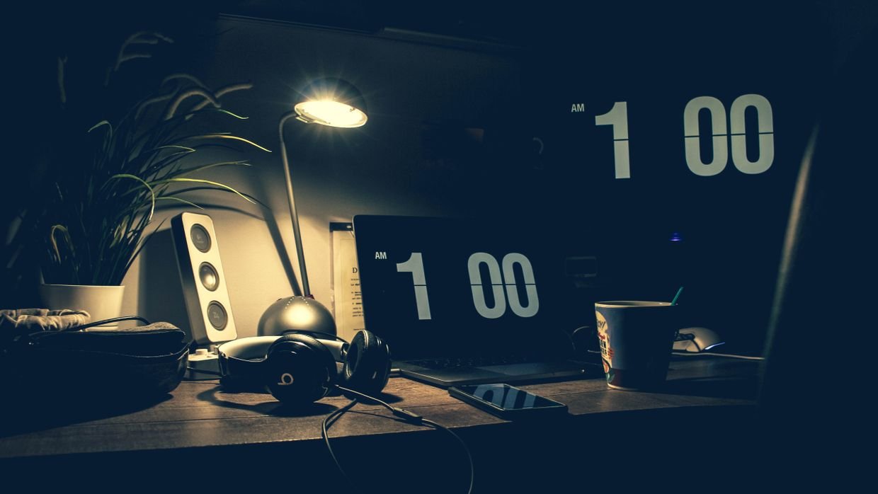 A clock on a desk beside a lamp, late in the evening.