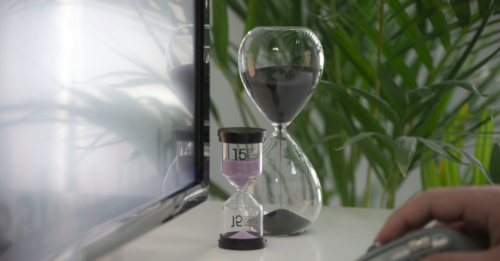 An hourglass beside a laptop, for waiting on YouTube to process automatic captions.