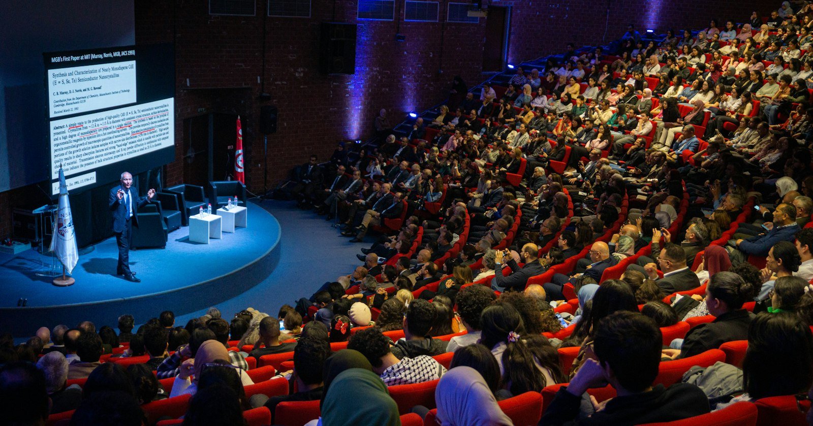 A speaker on stage in a large conference auditorium.