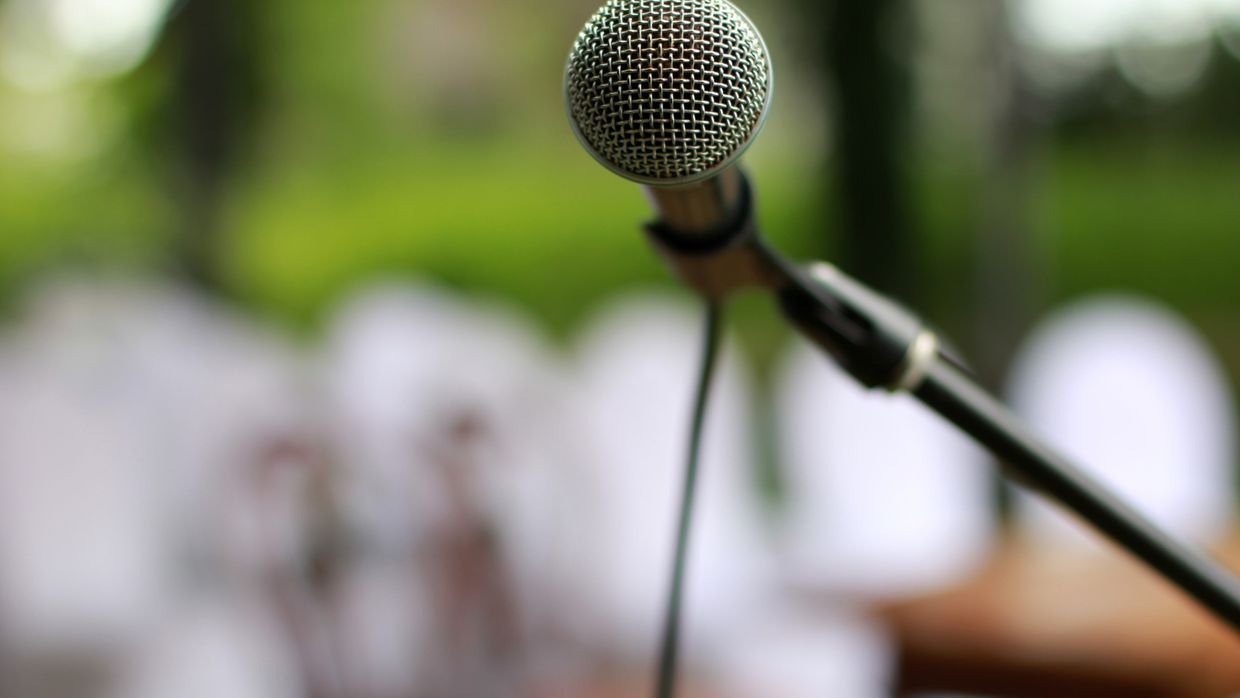 Microphones on a stage, where overlapping speakers blur together in unlabelled captions.