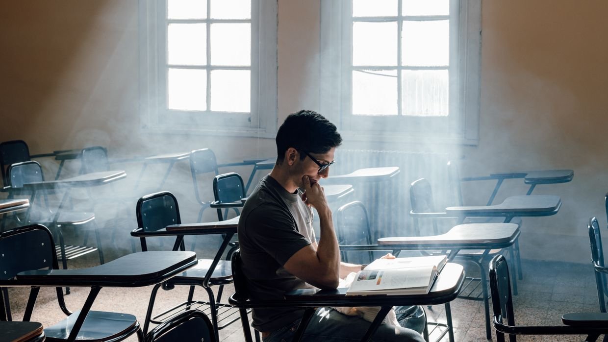 A student reading at a desk near a window.