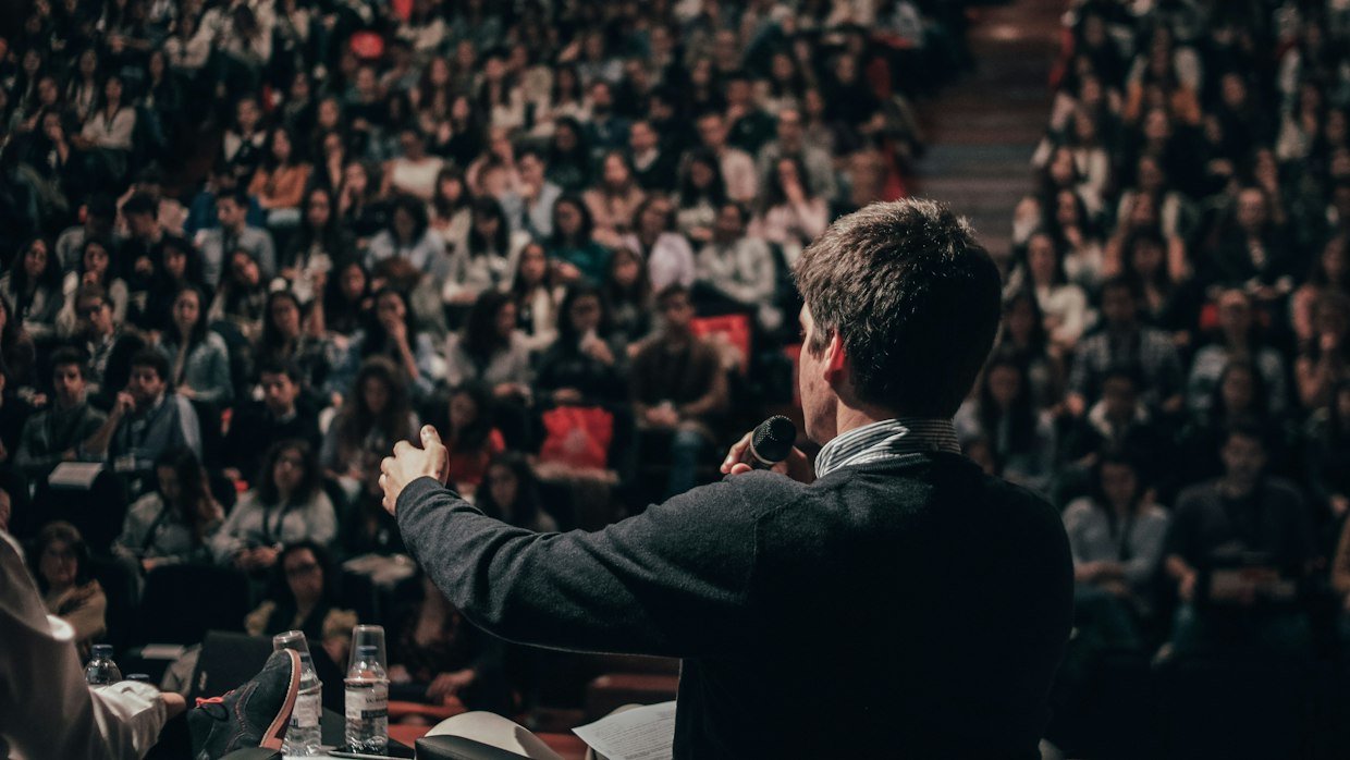 A speaker addressing a large seated audience.