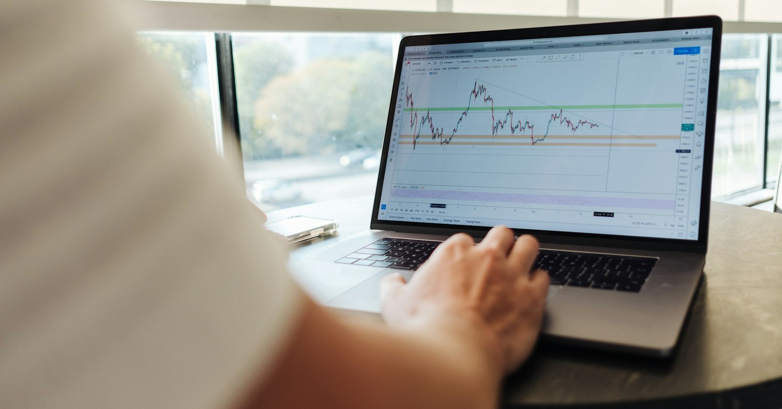 An investor taking notes while a market commentary video plays on a laptop.