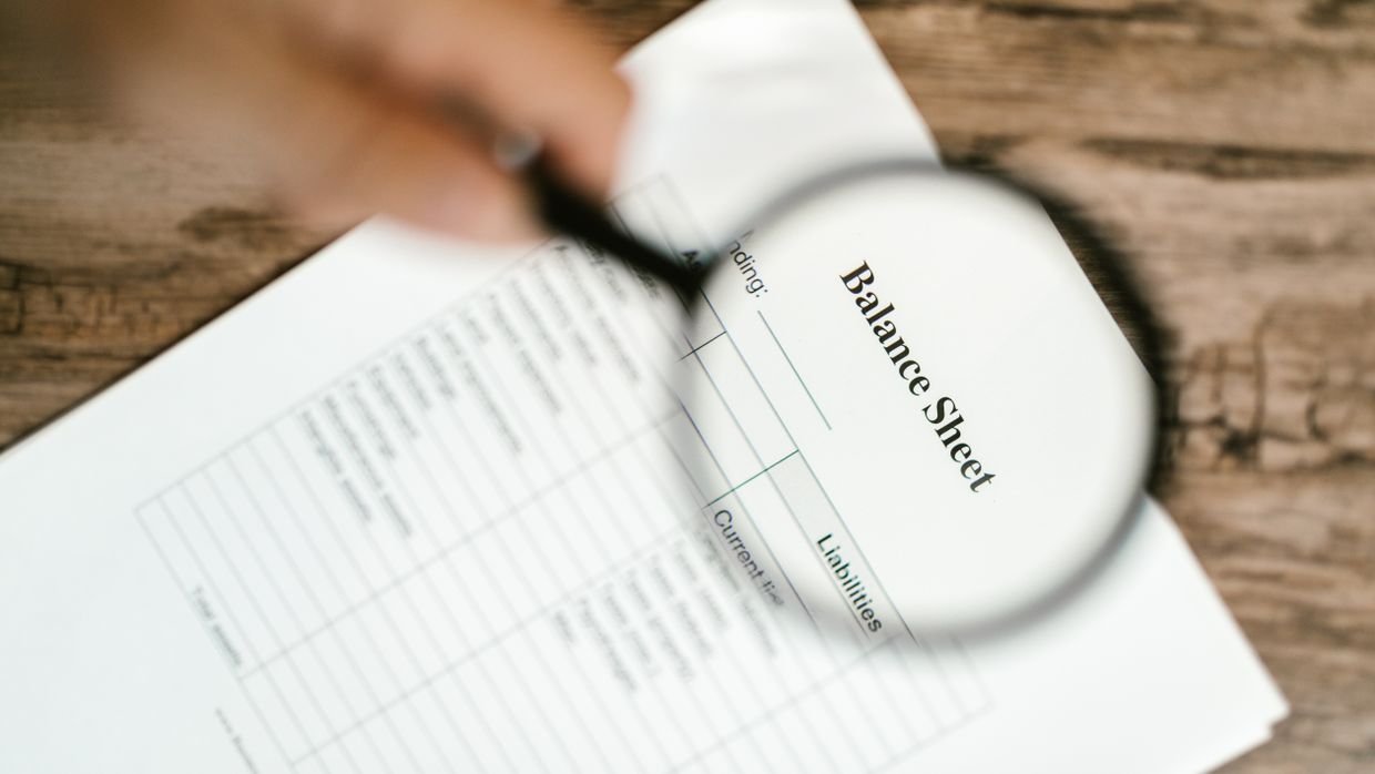 A magnifying glass over financial paperwork, a reminder that the summary reports claims and checks none of them.