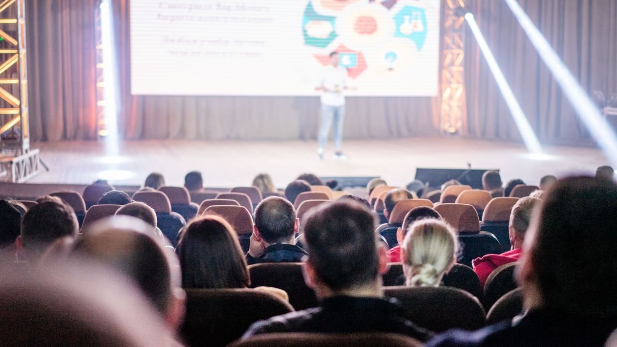 A speaker on stage in front of a full auditorium.