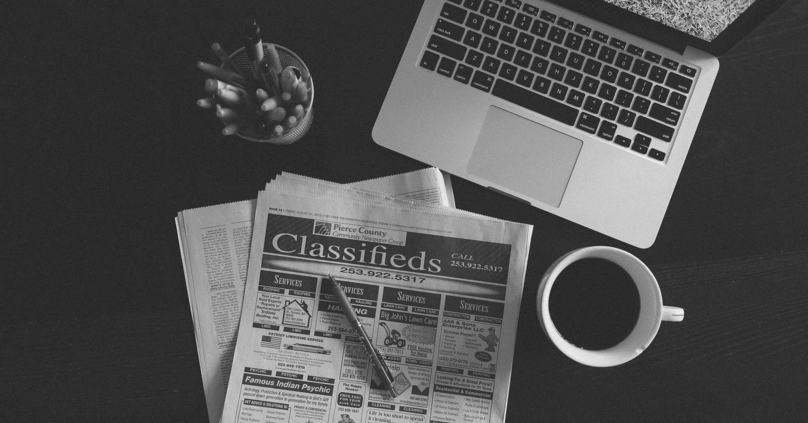 Newspapers beside a laptop on a desk.