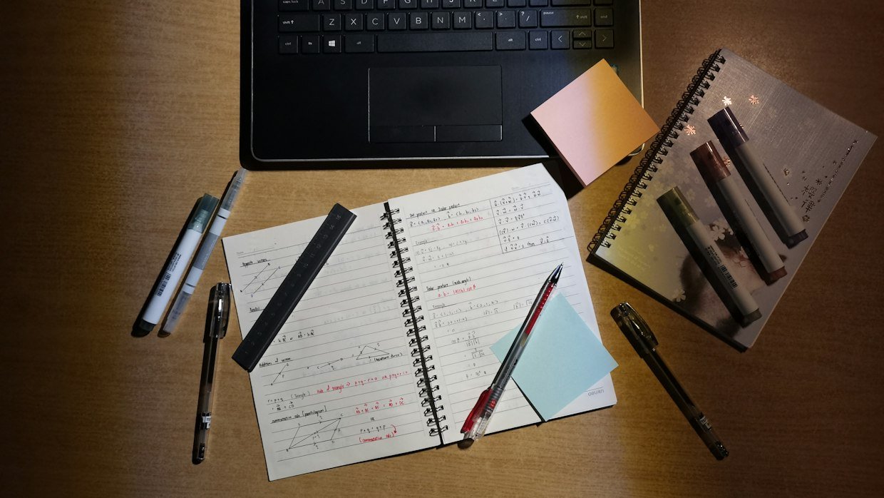 Notes written by hand next to a laptop, the step where a summary becomes an item in your own words.