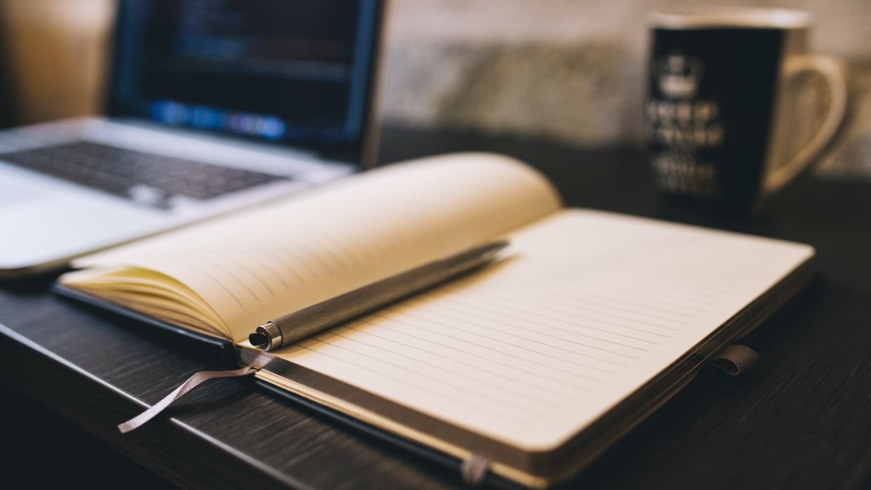 A handwritten notebook open beside a laptop.