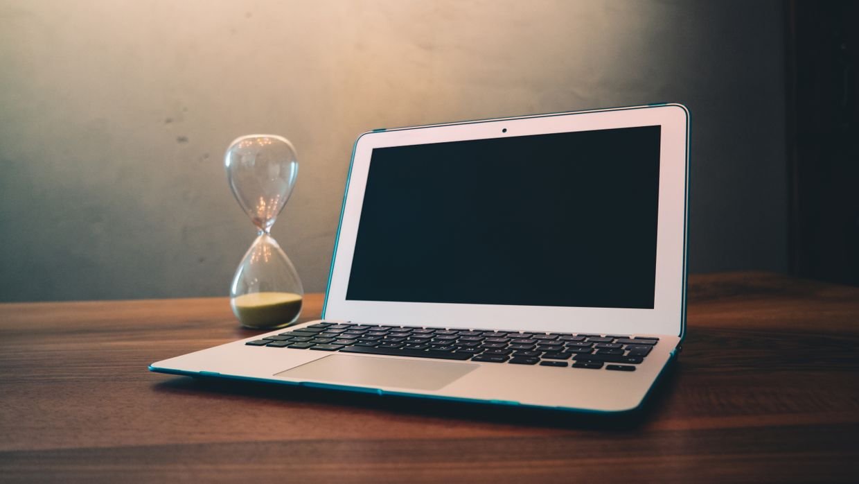 An hourglass standing beside a laptop.