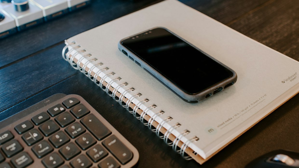 A phone and a notepad side by side on a desk.