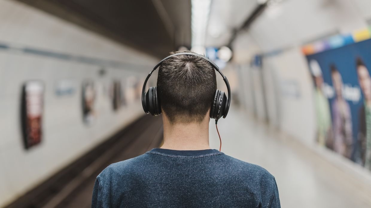 A commuter listening on headphones, for hearing a video rather than reading about it.