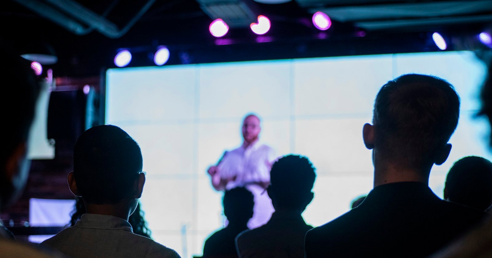 A speaker standing on stage under a spotlight.
