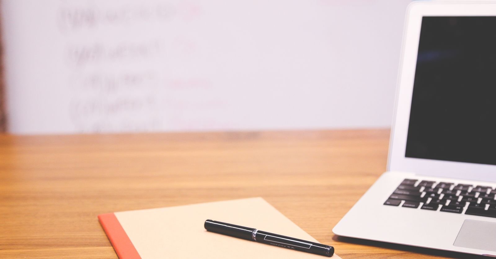 A notebook, pen and laptop on a desk.